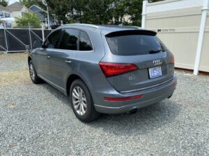 A gray suv parked in the gravel next to some trees.