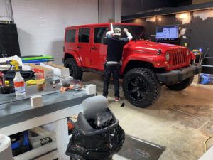 A man in black shirt standing next to red jeep.